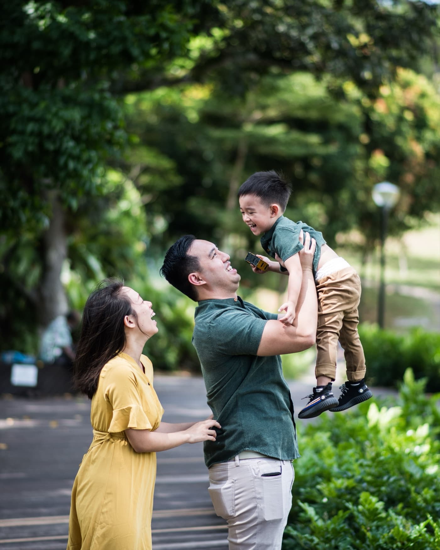 A family laughing together outdoors as a father lifts his young son